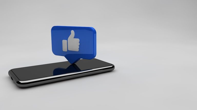 Image en 3D représentant un smartphone noir posé à plat, avec au-dessus un pictogramme bleu en forme de bulle contenant un pouce levé, symbole de “J’aime” sur les réseaux sociaux.